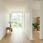 Porte a galandage entrouverte dans un couloir d'appartement renove, murs blancs et parquet chene clair
