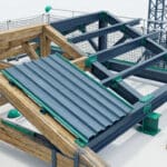 Vue en plongée d'une charpente hybride bois et métal en construction, avec des panneaux en bac acier posés.