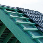 Structure de toiture en bois vert avec liteaux supportant des tôles imitation tuile gris anthracite.
