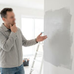 Un homme perplexe contemple une trace de peinture irrégulière sur un mur de maison en chantier.