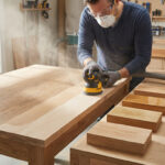 Un menuisier ponce une table en bois avec une ponceuse orbitale dans son atelier.