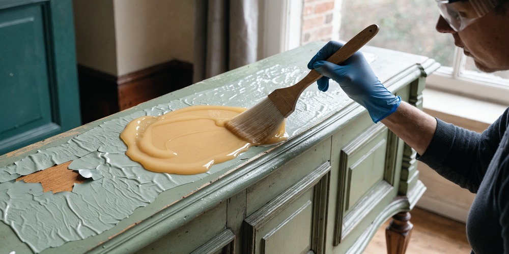 Décapant en gel appliqué au pinceau sur un meuble en bois peint, gants et lunettes de protection