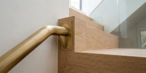 Main courante en laiton fixée par une platine au chêne de l'escalier, garde-corps en verre en arrière-plan