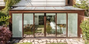 Véranda en aluminium à toit vitré accolée à une maison, vue depuis le jardin, avec ses grandes baies coulissantes