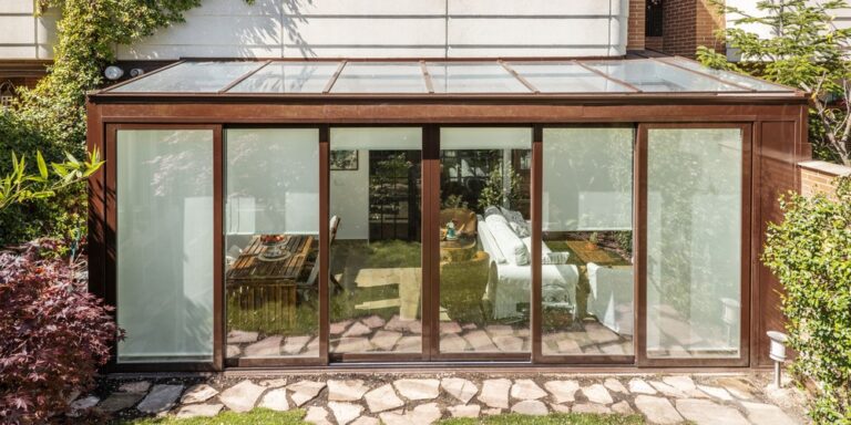 Véranda en aluminium à toit vitré accolée à une maison, vue depuis le jardin, avec ses grandes baies coulissantes