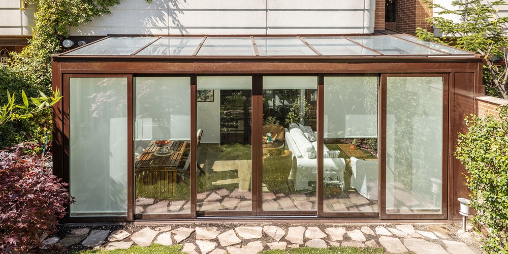 Véranda en aluminium à toit vitré accolée à une maison, vue depuis le jardin, avec ses grandes baies coulissantes